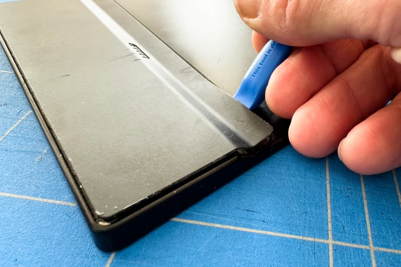 Sliding the plastic tool along the long side to unstick the back cover