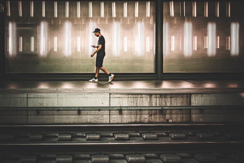 A man looking at his smartphone walking on the opposite plateform
